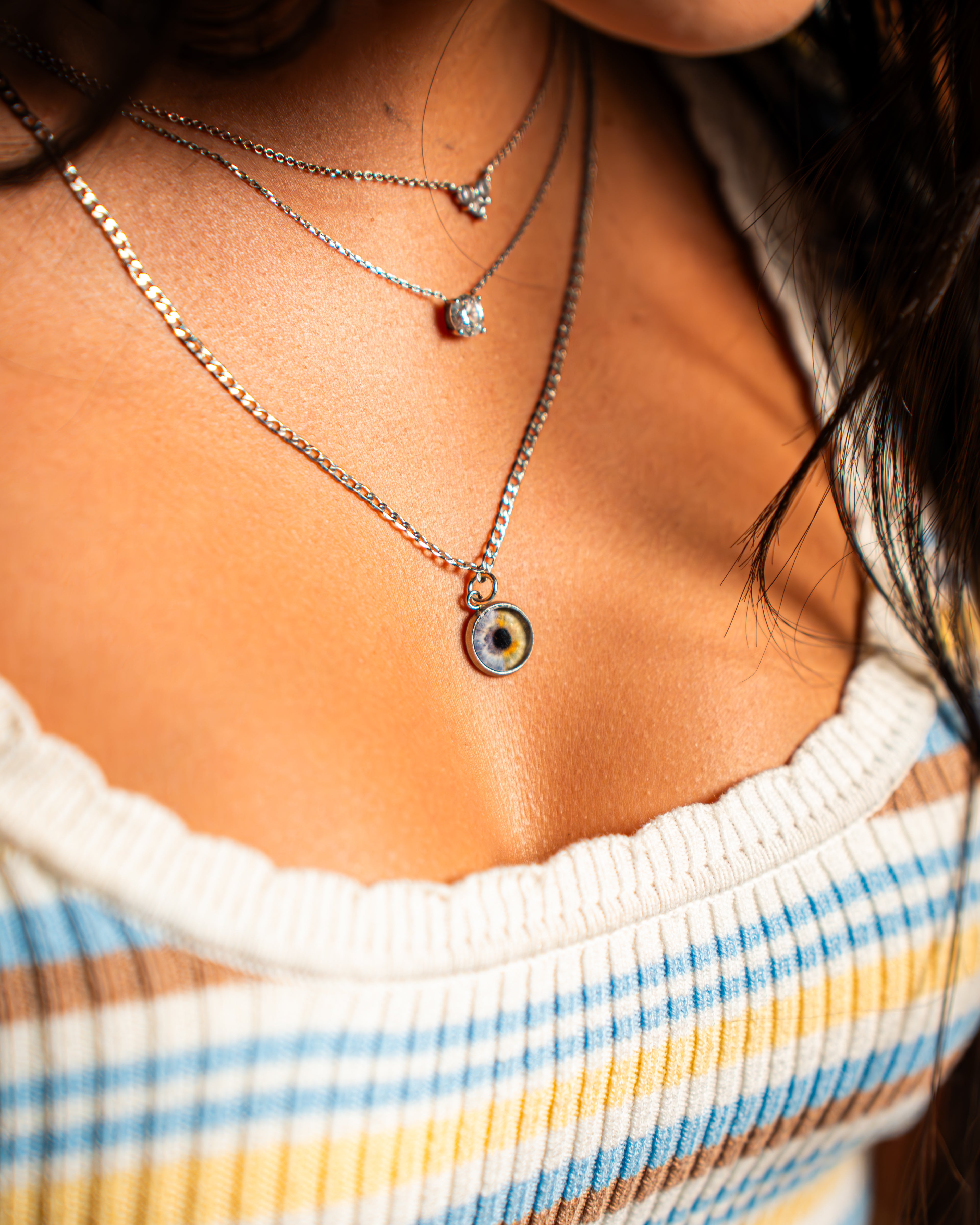 Close-up of a person wearing multiple necklaces with a focus on one with a small round pendant.