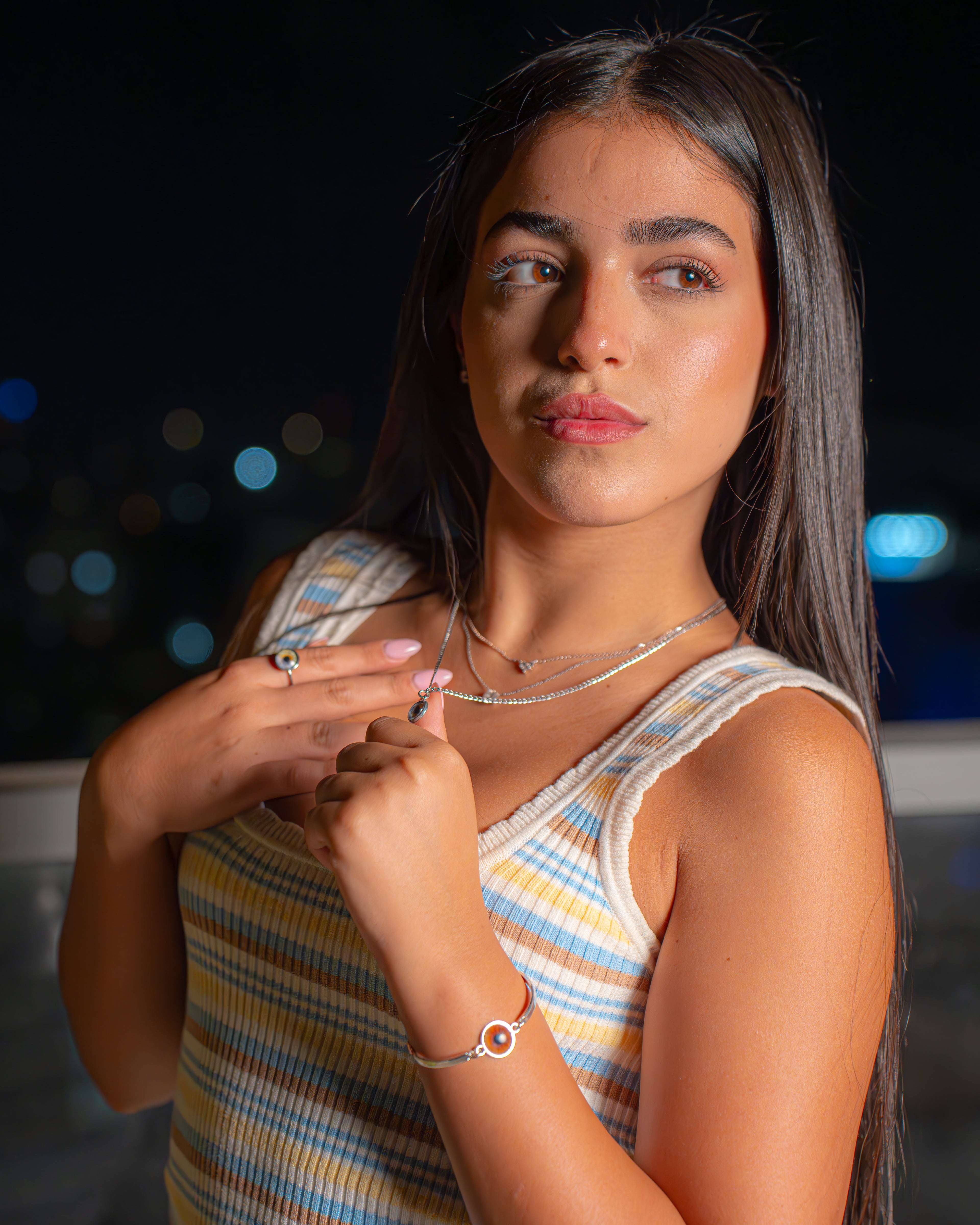 Woman wearing jewelry against a dark background with blurred lights